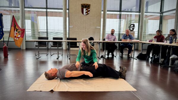 Oberbrandmeister Till erklärt bei der Brandschutzhelfer-Ausbildung die stabile Seitenlage anhand eines praktischen Beispiels mit einer Teilnehmerin.