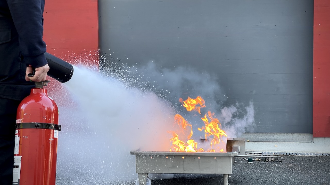 Reales Löschtraining bei einer Brandschutzhelfer Auffrischung mit Feuerlöscher und offenen Flammen.