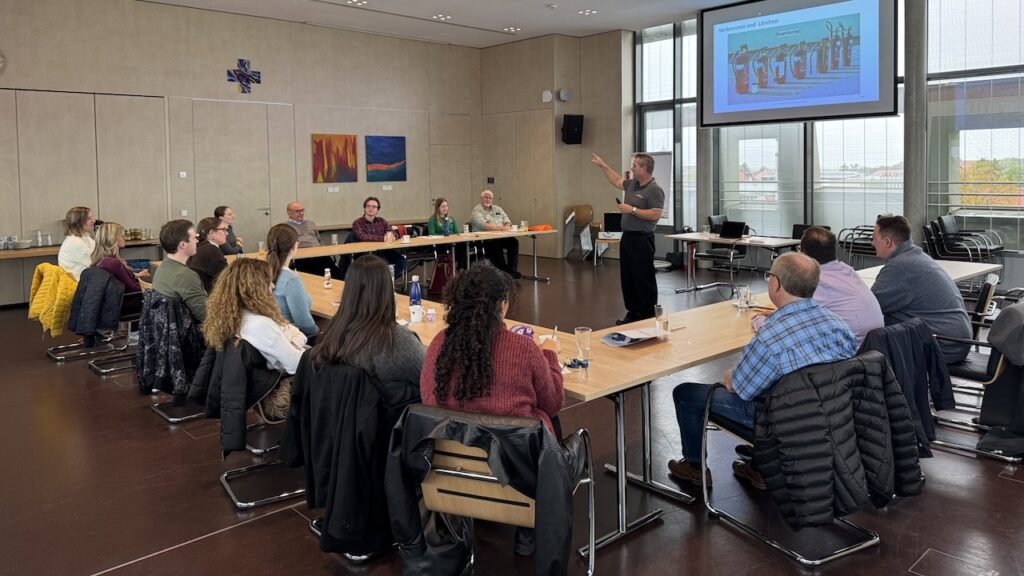 Inhouse-Brandschutzhelfer Auffrischung mit Berufsfeuerwehrmann im Seminarraum vor einer Gruppe Mitarbeitender während einer Schulung zu Feuerlöschern.