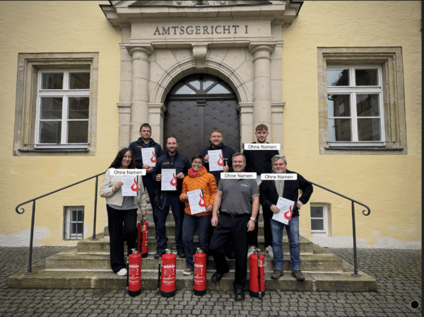 Gruppe frisch geschulter Mitarbeitender vor dem Amtsgericht, mit Feuerlöschern und Zertifikaten – offizieller Schulungsstandort in Baden-Württemberg.