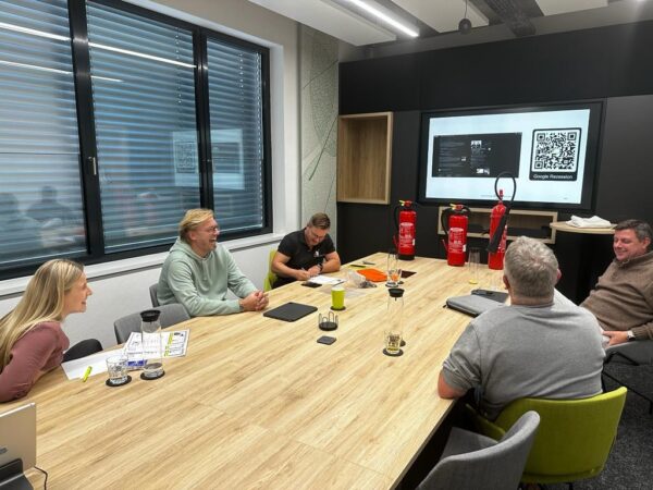 Berufsfeuerwehrmann erklärt Mitarbeitenden in einem modernen Firmenraum den richtigen Umgang mit Feuerlöschern.