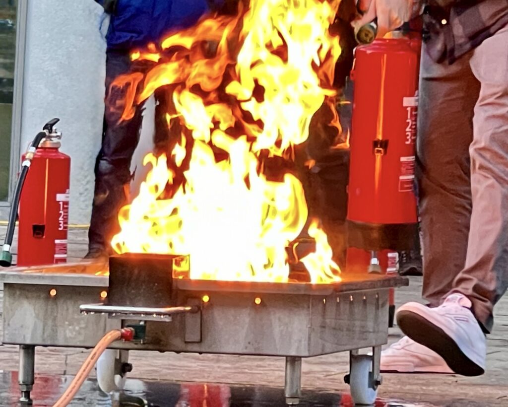 Echte Löschübung in der Brandschutzhelfer Ausbildung in Bayern – offenes Feuer am Brandsimulator mit Feuerlöschern, durchgeführt durch Berufsfeuerwehrmänner.