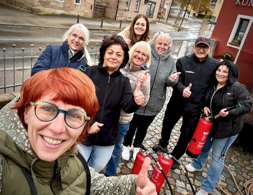 Gruppe zufriedener Teilnehmender nach der Brandschutzhelfer Schulung in Bayern – mit Feuerlöschern und positiver Rückmeldung.