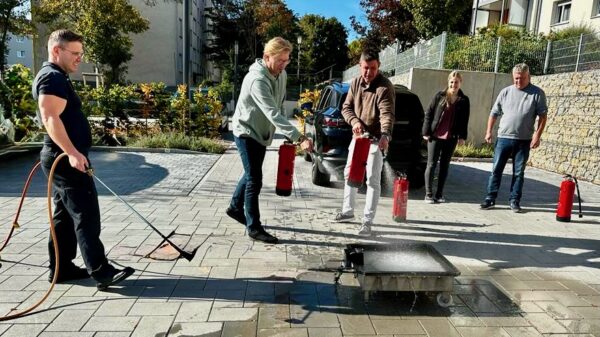 Teilnehmende einer Brandschutzschulung im Betrieb üben unter Anleitung von Berufsfeuerwehrmännern den Umgang mit dem Feuerlöscher.