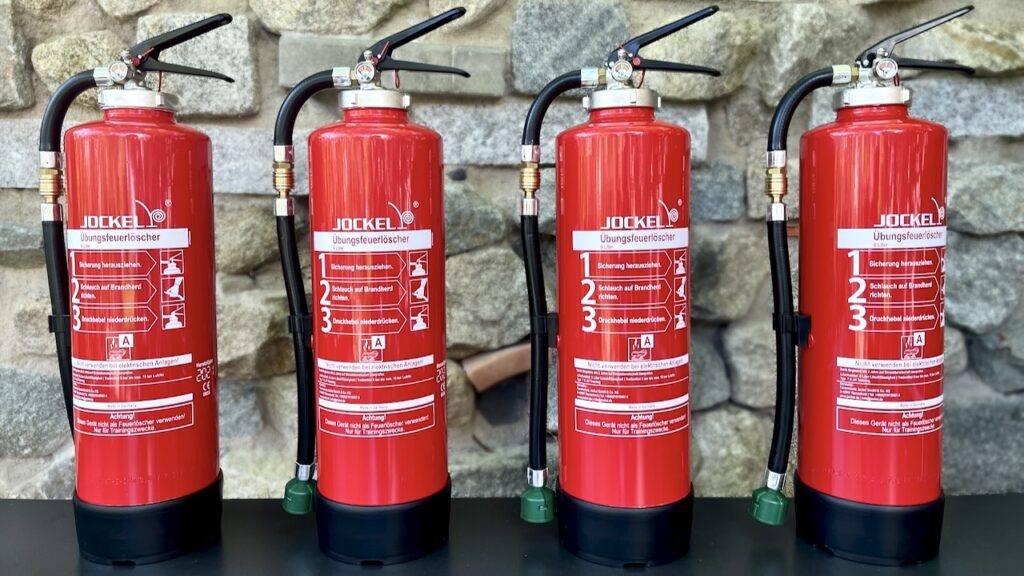 Vier rote Feuerlöscher auf schwarzem Tisch vor Steinwand – Feuerlöscher Bild kostenlos