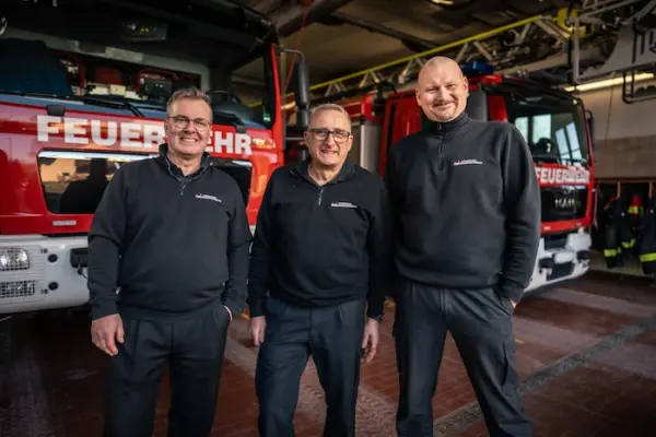 Ausbilder-Team von Lehrgang-zum-Brandschutzhelfer.de vor Feuerwehrfahrzeugen in einer Feuerwache – Brandschutzhelfer Ausbildung durch Berufsfeuerwehr-Ausbilder