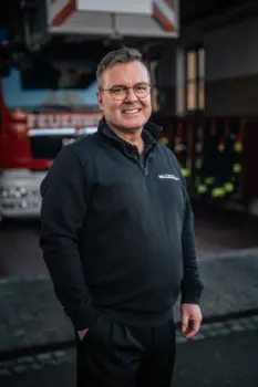 Thomas Till, Oberbrandmeister der Berufsfeuerwehr, Ausbilder für Brandschutzhelfer mit Einsatz- und Leitstellenpraxis vor einer Drehleiter