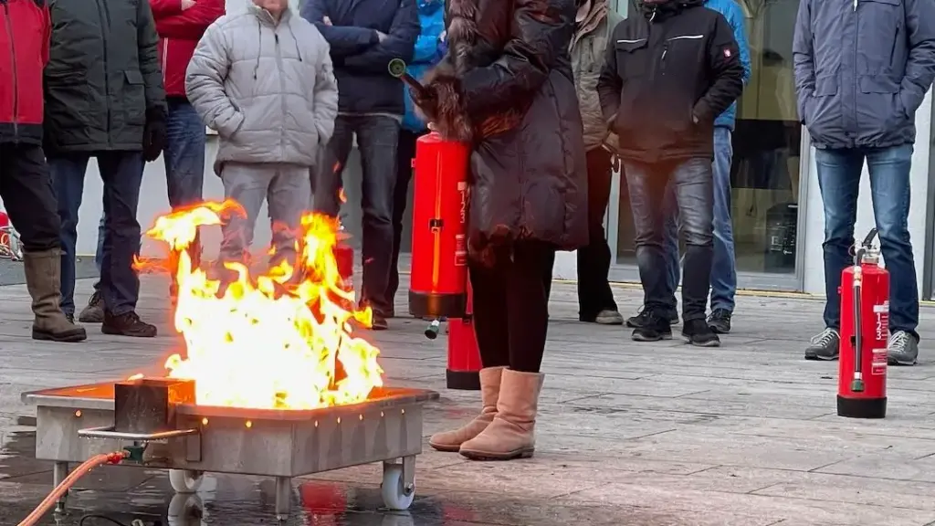 Teilnehmerin einer Brandschutzhelfer-Ausbildung steht mit Feuerlöscher vor einem Entstehungsbrand und bereitet sich auf den Löschversuch vor.