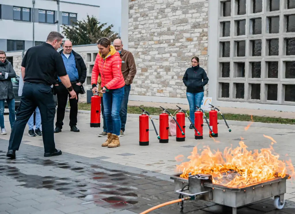 Brandschutzhelferin beginnt unmittelbar nach Erkennen eines Entstehungsbrandes mit einem Löschversuch und setzt einen Feuerlöscher ein.