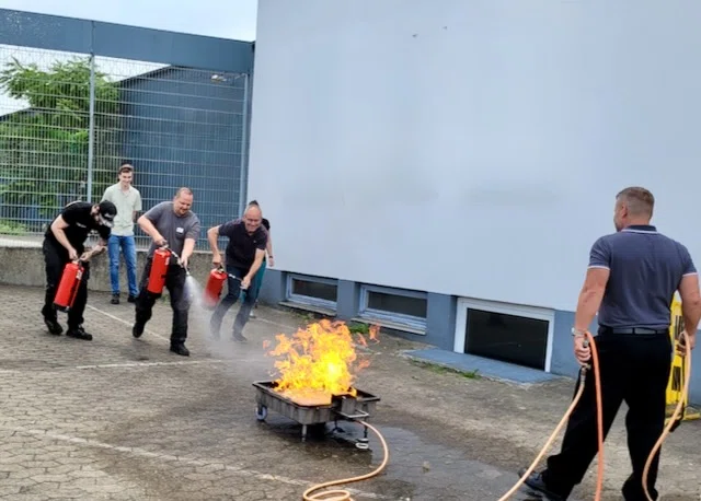 Umgang mit Feuerlöschern: Mehrere Brandschutzhelfer setzen bei einer praktischen Löschübung gleichzeitig Feuerlöscher gegen einen Entstehungsbrand ein.