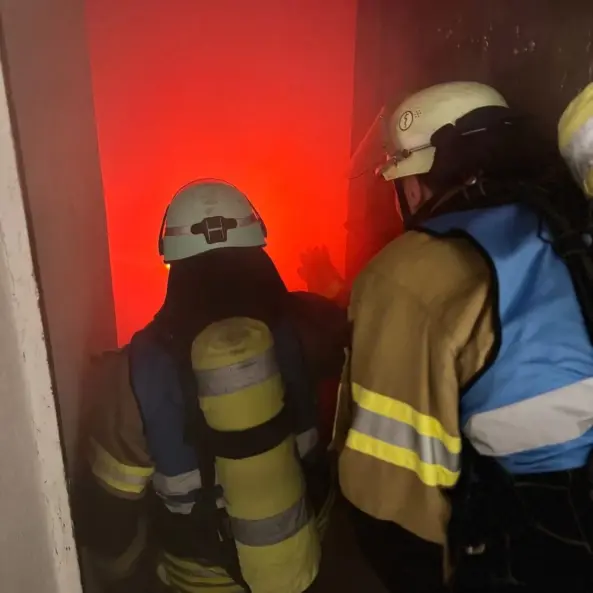 Berufsfeuerwehrbeamte unter Atemschutz beim Innenangriff vor einem von Feuerschein erhellten Raum
