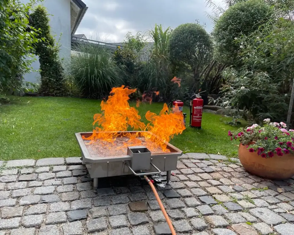 Brandsimulator für einen Brandschutzhelfer-Kurs auf einer befestigten Gartenfläche ohne Brandflecken oder Löschmittelrückstände