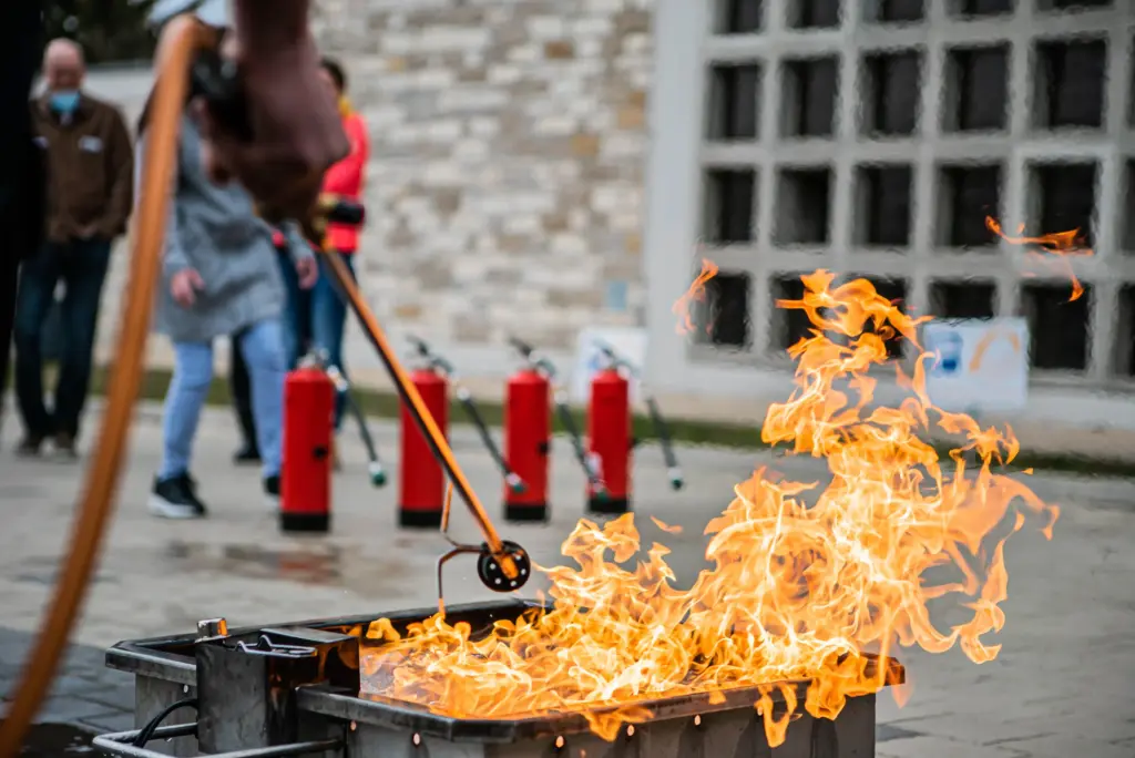 Ein Teilnehmer löscht bei einer Brandschutzhelfer Auffrischung mit einem Feuerlöscher ein echtes Übungsfeuer. Im Hintergrund stehen weitere Feuerlöscher für die praktische Löschübung bereit.