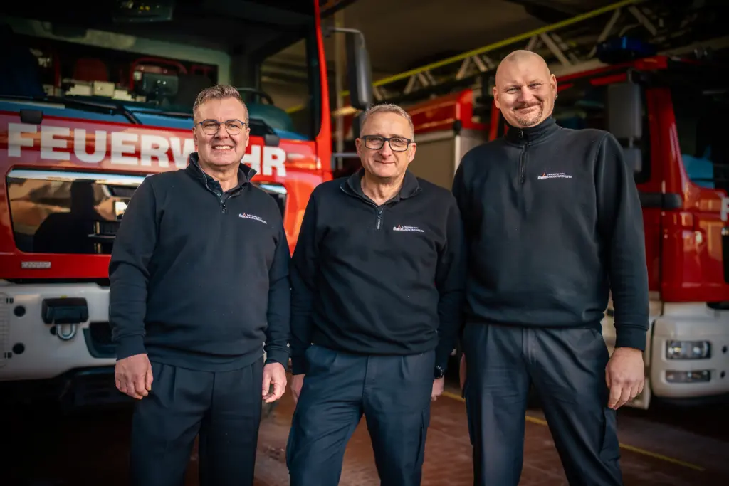 Die Ausbilder Thomas Till, Heiko Schmidt und Uwe Wahl als aktive Berufsfeuerwehrmänner vor Feuerwehrfahrzeugen