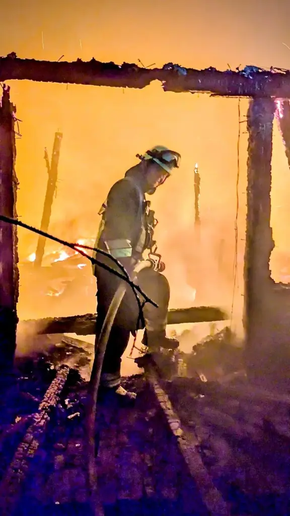 Berufsfeuerwehrmann in einer ausgebrannten Gebäudekonstruktion vor starkem Feuerschein