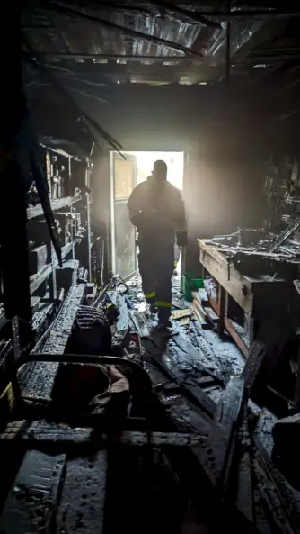 Berufsfeuerwehrmann in einem stark ausgebrannten und verrußten Innenraum nach einem Gebäudebrand