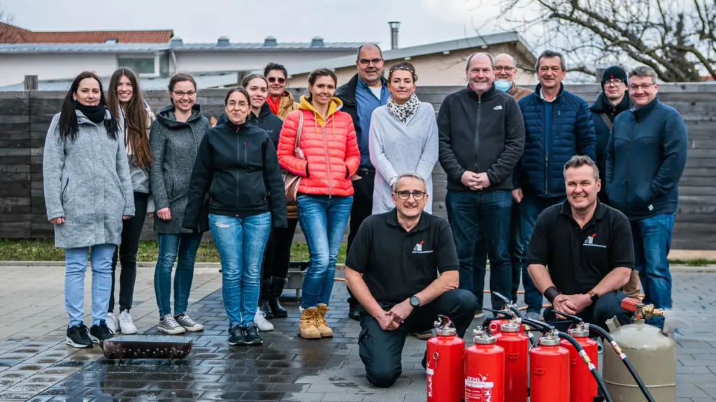 Mitarbeitergruppe mit Ausbildern, Feuerlöschern und Übungstechnik bei einer gemeinsamen Brandschutzschulung im Betrieb