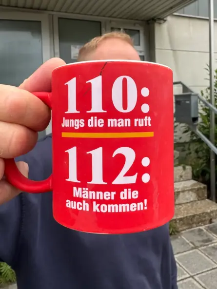 Thomas Till mit humorvoller 112-Tasse als persönlicher Bezug zur Tätigkeit in der Integrierten Leitstelle