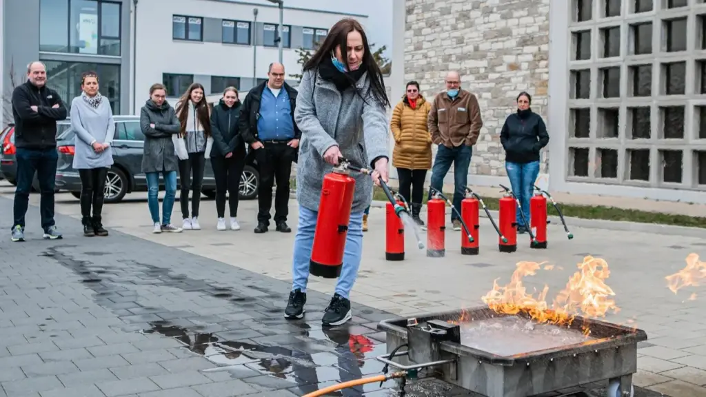 Teilnehmerin bei einer Brandschutzhelfer-Ausbildung im Betrieb in Baden-Württemberg während einer praktischen Löschübung mit Feuerlöscher.