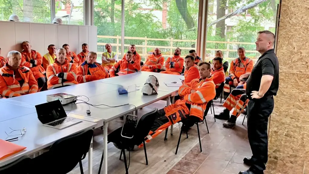 Mitarbeitende in Warnschutzkleidung bei der Theorie einer Brandschutzhelfer-Ausbildung im Rohbau einer Baustelle
