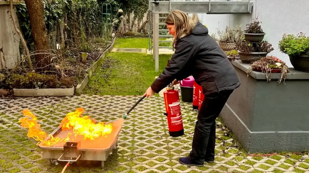 Brandschutzhelfer-Schulung in der Nähe: Teilnehmerin bei der Löschübung mit Feuerlöscher und Brandtrainer vor Ort im Betrieb